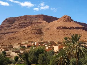 A cluster of small simple buildings in the desert, with brown hills in the background and shrubbery in the foreground.