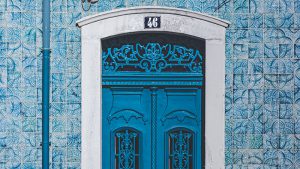 Puerta verde azulado con detalles ornamentales, rodeada de azulejos blancos y verde azulado.