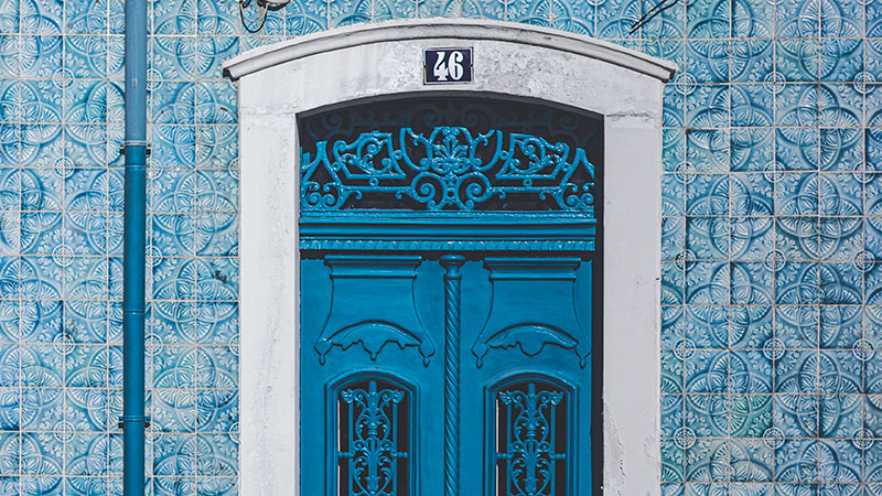 Teal door with ornate detail, surrounded by teal and white ornate tiles.