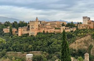 Alhambra along a hill top, surrounded by green shrubbery.