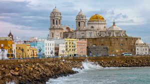 The sea crashes against a rocky wall with the Cadiz Cathedral rising up beyond.
