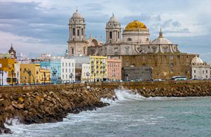 The sea crashes against a rocky wall with the Cadiz Cathedral rising up beyond.