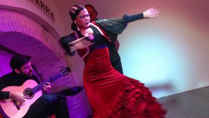 Flamenco dancer in a red dress, and a seated guitarist on the left.