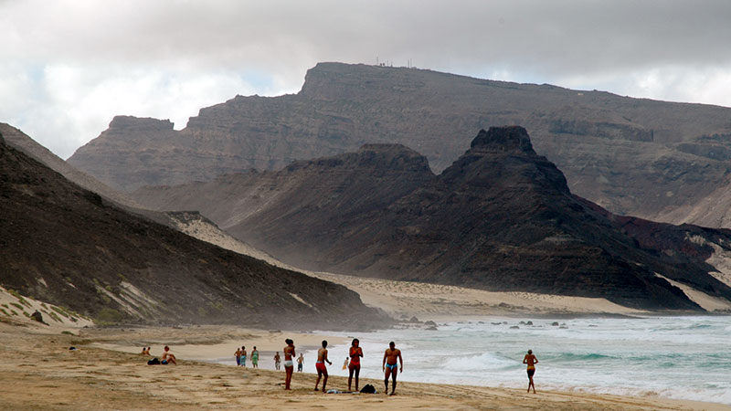 Beach with people near the water, with dark hills in the background