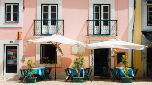 Tables with white umbrellas outside a pink-painted cafe.