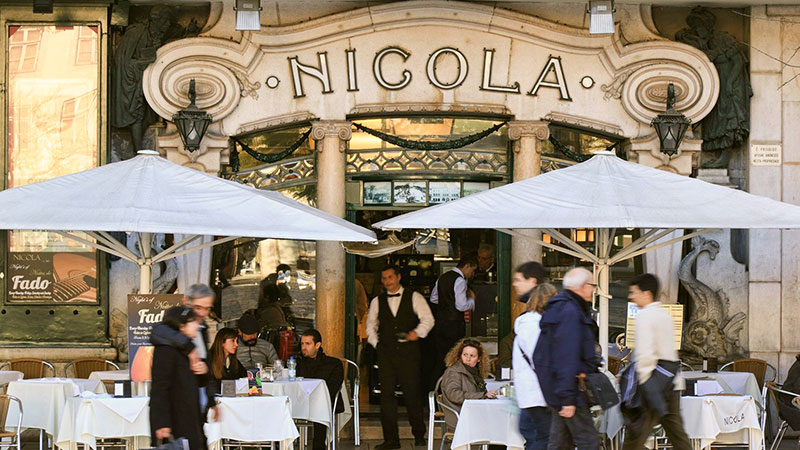 Asientos al aire libre bajo sombrillas blancas frente al café Nicola en Lisboa.
