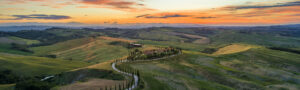 A winding road meanders through green hills in the Tuscany sunset