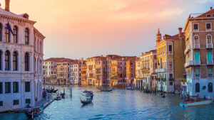 The Grand Canal at sunset with gondolas floating in front of brightly-lit hotels