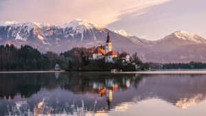 Bled castle against a backdrop of snow-covered mountains with Bled lake in the foreground