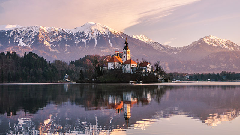 Bled castle against a backdrop of snow-covered mountains with Bled lake in the foreground