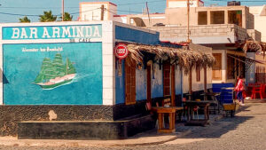 Bar Arminda building with a mural depicting a sail boat and a grass awning over a few outdoor tables and chairs.