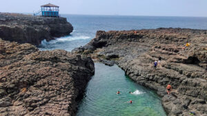 Large rocky cliffs form a swimming hole near the sea shore.
